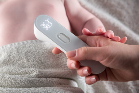 Close Up of mother hand taking temperature measurement of infant baby with high temperature by hi...