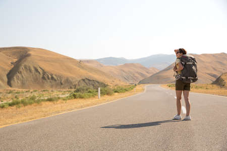 Hitchhiker traveler woman on the road in sunset. Girl traveler hiker on the road. Summer vacation. Freedomの写真素材