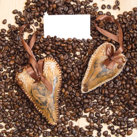 two decorated hearts on the background of coffee beans with card for textの写真素材