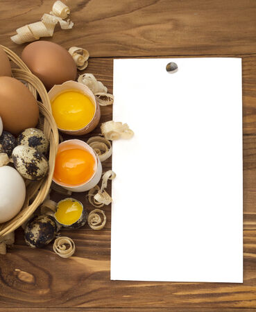 chicken and quail eggs on wooden background with paper for textの写真素材