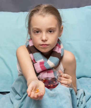 Sick child with pills and a cup of herbal tea in hands sitting in bedの写真素材