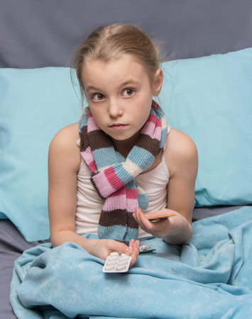 Sick child with pills in hands sitting in a bedの写真素材
