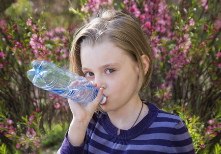Little schoolgirl  drinks water from a plastic bottle outdoors in springの写真素材
