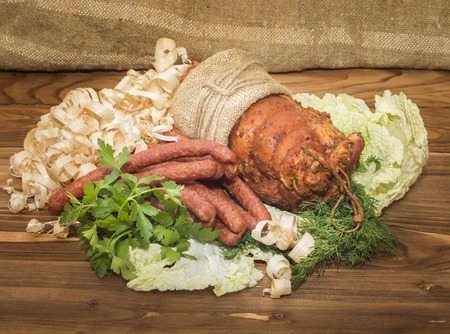 Baked pork and sausages hunting on wooden table with fresh herbs and garlicの写真素材