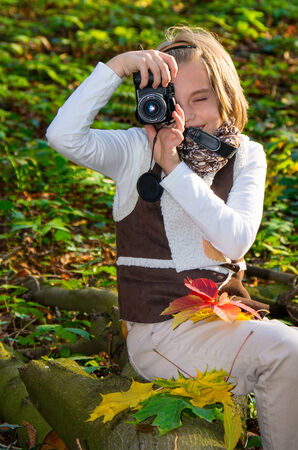 Happy little girl with a camera in autumn park.の写真素材