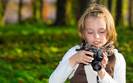 Happy little girl with a camera in autumn park.の写真素材