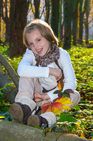Portrait of a happy little girl with colored maple leaves in autumn park.の写真素材