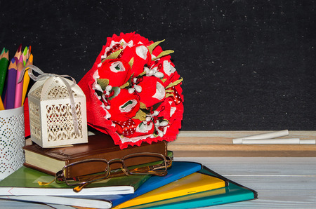 Teacher  Day. Flowers and gift, copybooks on the teacher's desk. (flowers, gift; glasses, copybooks, board, pencils).の写真素材