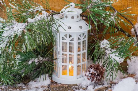 Decorative lantern burning in the snow with a conifer branch in winter dayの写真素材
