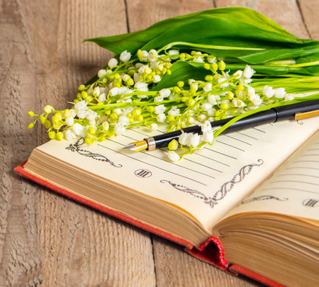 Flowers lily of the valley on the book for records and a pen on a wooden background. Soft focus, deliberate slight blurring .の写真素材
