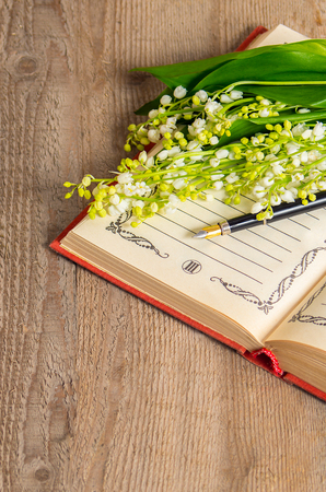 Flowers lily of the valley on the book for records and a pen on a wooden backgroundの写真素材