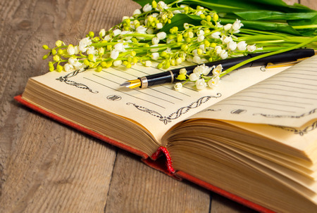 Flowers lily of the valley on the book for records and a pen on a wooden background. Soft focus, deliberate slight blurring .の写真素材