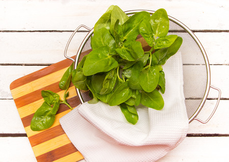 Fresh spinach leaves in basket  on a white wooden background.の写真素材