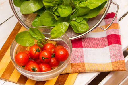 cherry tomatoes on the plate and fresh spinach in a basket on a wooden tableの写真素材