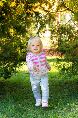adorable happy baby girl with blond hair walking in the park on a sunny autumn afternoonの写真素材