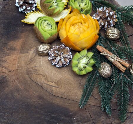 composition of fresh carved fruits decorated with fir branches and nuts on a wooden backgroundの写真素材