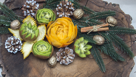 composition of fresh carved fruits decorated with fir branches and nuts on a wooden backgroundの写真素材