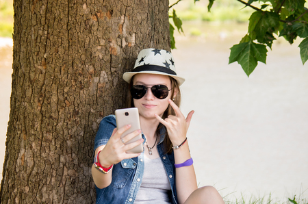 happy teenage girl with glasses and hat to make selfie in nature backgroundの写真素材