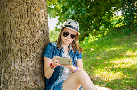 happy teenage girl with glasses and hat to make selfie in nature backgroundの写真素材