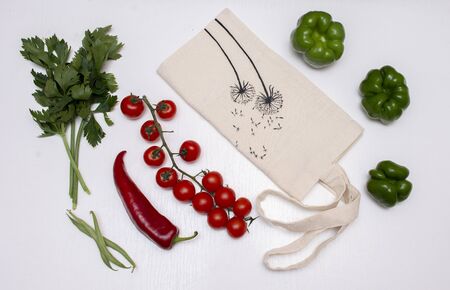 Vegetables with beige eco bags on a white wooden background. Celery, chili pepper, cherry tomatoes, beans. Zero waste concept.の写真素材