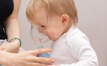 Little toddler girl with asthma and allergies makes inhalation in a mask with medication through a nebulizer on a gray backgroundの写真素材