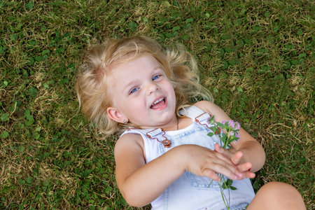 Happy blond girl lying on the green grass and smiling sincerely. happy childhood.