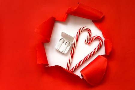 Christmas shopping online concept. White wireless headphones with candy in the form of a heart on a red background. Gift for the holidays. Red banner space for text. Winter sales, discounts.の写真素材