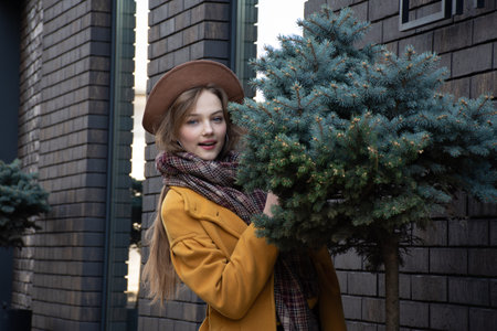 Girl in a yellow coat and beret with a Christmas tree in her hands.の写真素材