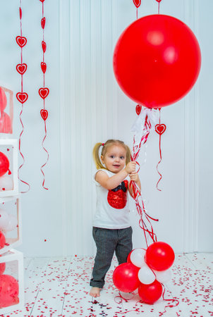 Cheerful little girl holding a red balloon on a white background. Valentine's Day.の写真素材