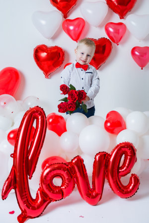 portrait of a blond boy with a bouquet of roses and the inscription love on Valentine's Day on a white background of heart-shaped balloonsの写真素材