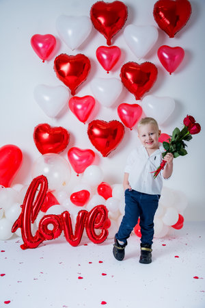 toddler boy standing with bouquet of roses flowers for Valentine's Day on background with heart shaped balloons and love inscription.の写真素材