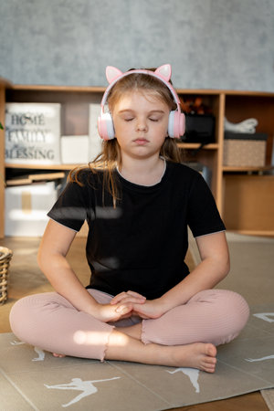 Little cute girl in headphones practicing yoga poses on mat at homeの写真素材