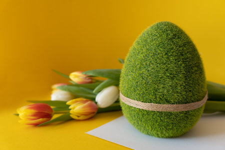 Easter composition on a yellow background. Green Easter egg with tulips on a blurred background with...
