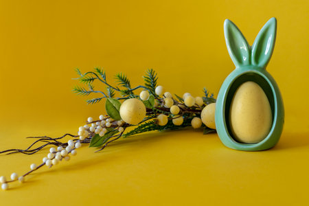 Easter composition on a yellow background. Egg with bunny ears and a branch and Easter eggs with space for text.の写真素材