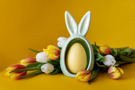 Easter concept. Egg with rabbit ears and tulips on a yellow background with space for text.の写真素材