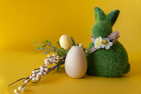 Easter concept. Green Easter bunny with a branch with Easter eggs on a yellow background with space for text.の写真素材