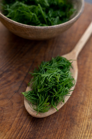 Concept of aromatic herbs for cooking. Chopped fresh dill with a wooden spoon on a brown kitchen board background. Preparing to freeze.の写真素材