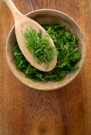 Freshly picked chopped fresh dill on a wooden spoon in a bowl with dill on a wooden background. Concept of aromatic herbs for cooking.の写真素材