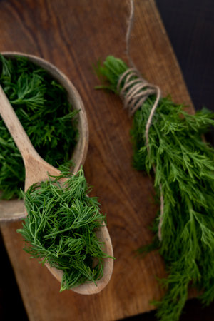 Chopped fresh dill on a wooden spoon on a background of a kitchen board and a pile of dill in a plate. Preparing for freezing. Concept of aromatic herbs for cooking.の写真素材
