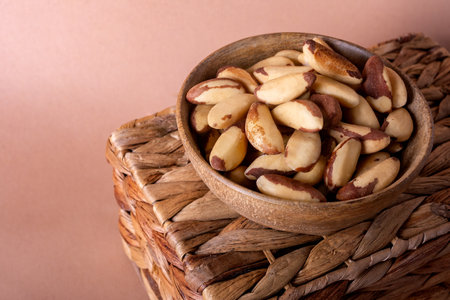 Shelled Brazil nuts in a wooden bowl close-up on a wicker basket and a mocha background with space for text.の写真素材