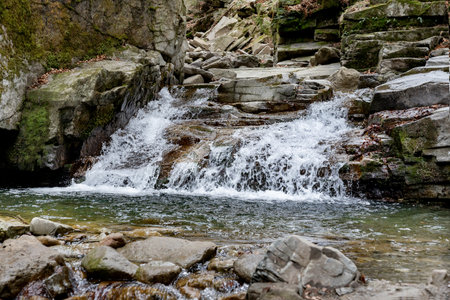 Landscape in the forest with a waterfall among the rocks. Natural stream in the mountains. Wild waterfall in the spring in a pine forest among the rocks.の写真素材