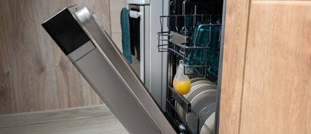 Open dishwasher with light dishes, blue glasses and air freshener on wooden kitchen background. Water-saving and energy-efficient household appliances.の写真素材