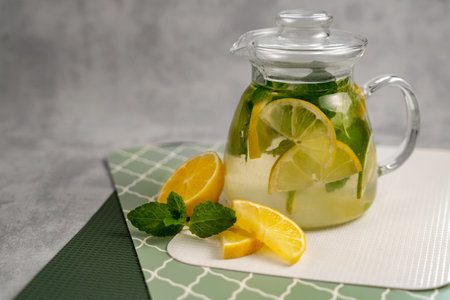 Refreshing lemon-mint drink in a glass teapot on a green patterned surface. Summer drinks concept. Food photo for catalog, publications, magazines.の写真素材