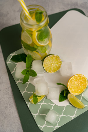 Process of making citrus detox tea with lime, lemon, mint and ice cubes on a green patterned gray surface with space for text. Concept of making summer lemonades.の写真素材