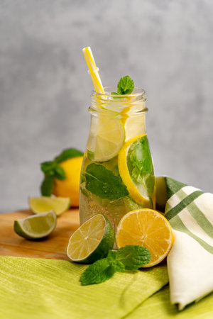 Cold lemonade in a glass jar with a straw with slices of lime, lemon, mint on a blurred gray background. Concept of making summer lemonade. Cold drinks.の写真素材