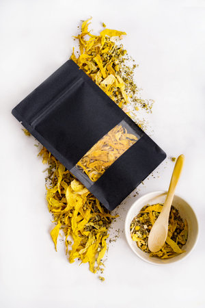 Black herbal tea packaging, mockup. Soothing tea blend with dry yellow leaves and flowers scattered under the packaging on a light background. Healthy drinks concept.の写真素材