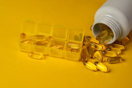 Organizer with Omega-3, Omega-9 capsules and a white bottle from which the capsules are poured. Organizer for dietary supplements. Medicine and pharmacology.の写真素材