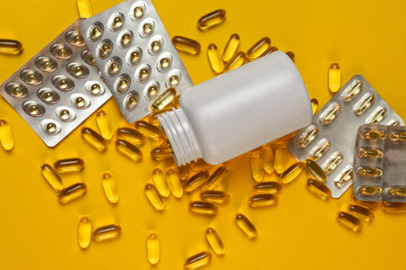 Scattered blister packs and a jar of capsules of dietary supplement omega-3, omega-9 on a yellow...