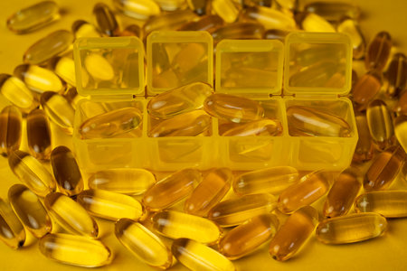 Close-up of an organizer with yellow Omega-3 or Vitamin D capsules on scattered capsules. Organizer for dietary supplements. Medicine and pharmacology.の写真素材