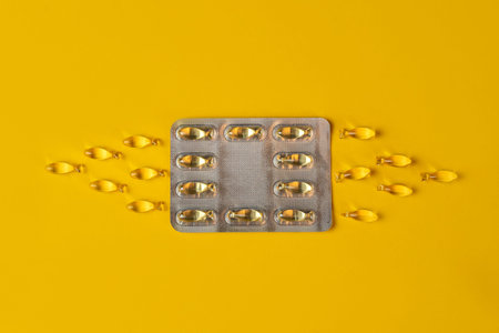 Blister pack of Omega-3 or vitamin D capsules in the shape of a fish on a yellow background,...